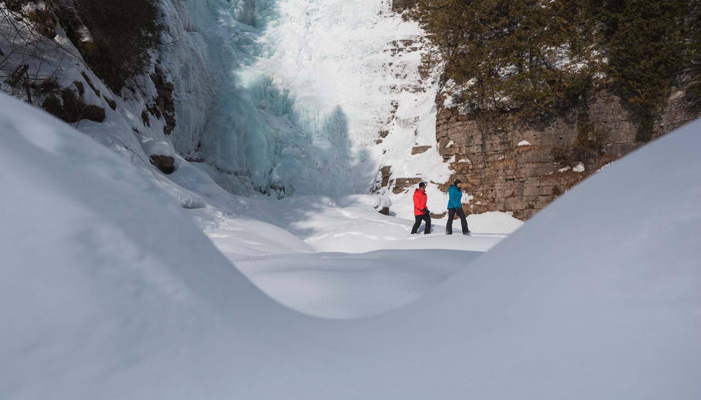 Two hikers walk in the snow at the foot of an icy waterfall, near Québec City.