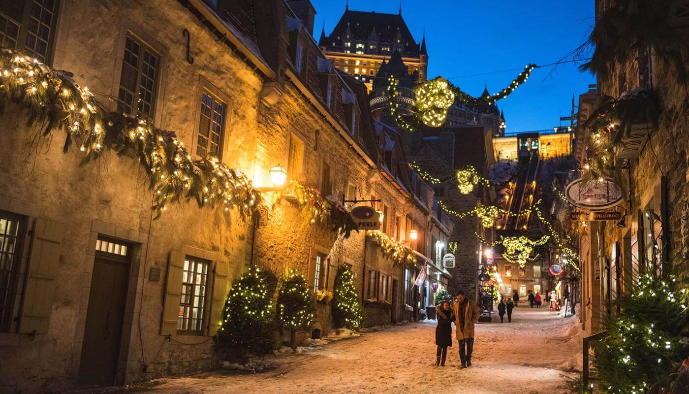 Un couple amoureux marche en soirée dans la rue du Petit-Champlain illuminée pour Noël et le temps des fêtes. 