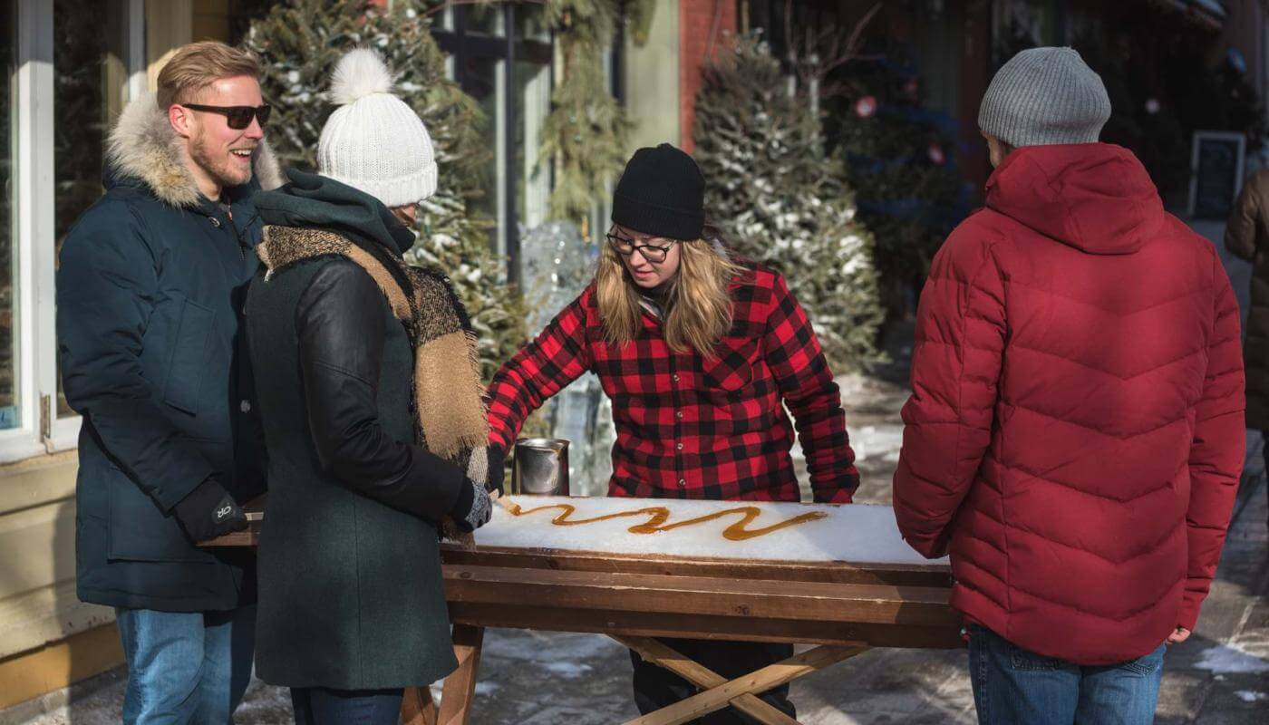 Three people stop in the Petit-Champlain district to taste taffy on snow in a small sugar shack.