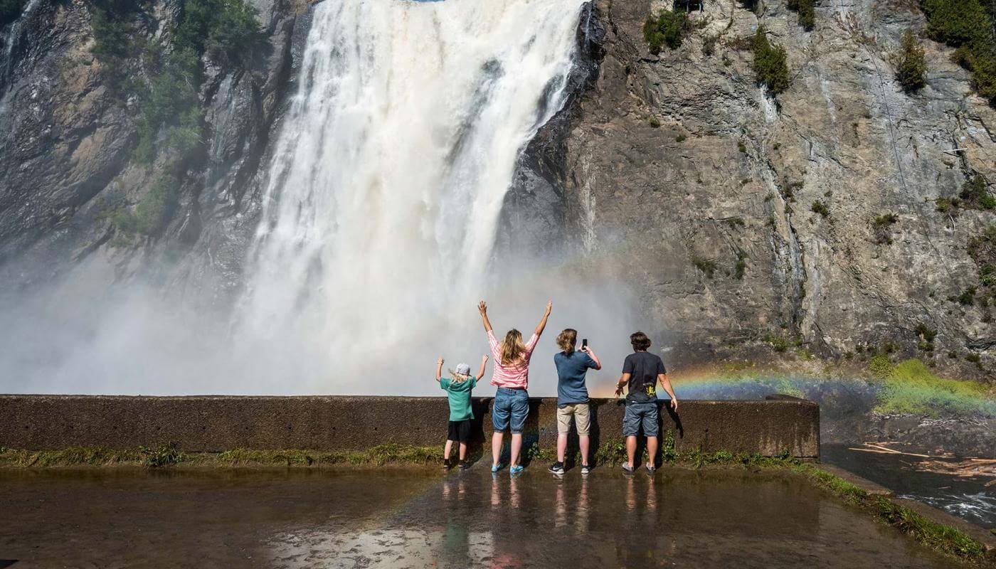A family gets watered at the foot of the waterfall, in Chute-Montmorency Park, in summer.