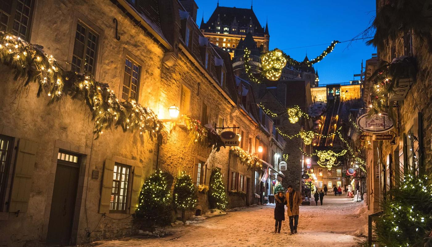 Un couple amoureux marche en soirée dans la rue du Petit-Champlain illuminée pour Noël et le temps des fêtes. 