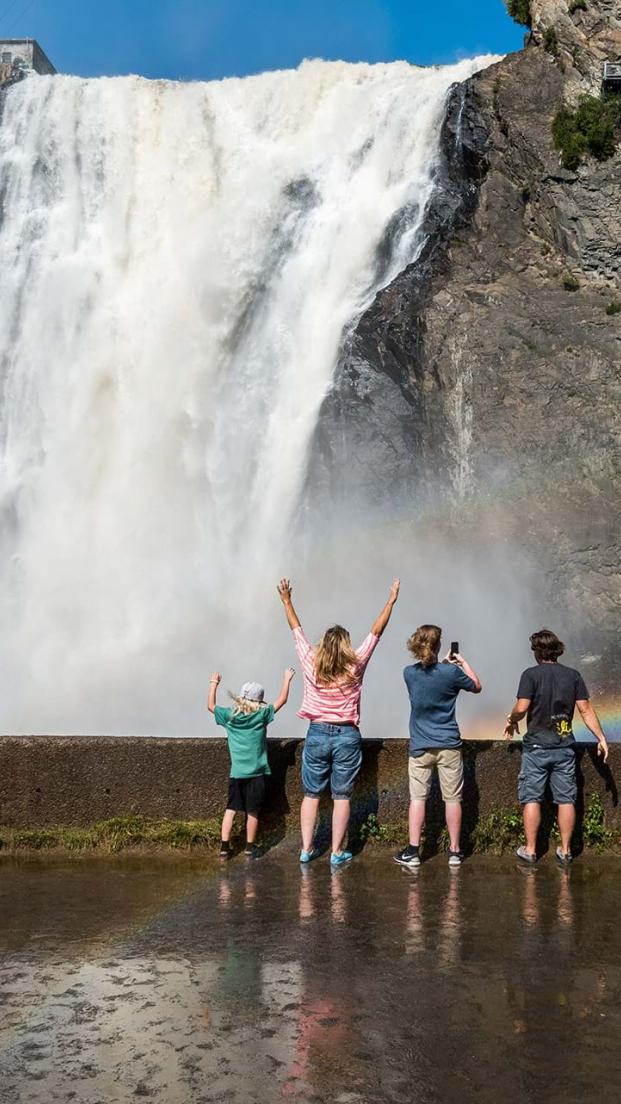 A family gets watered at the foot of the waterfall, in Chute-Montmorency Park, in summer.