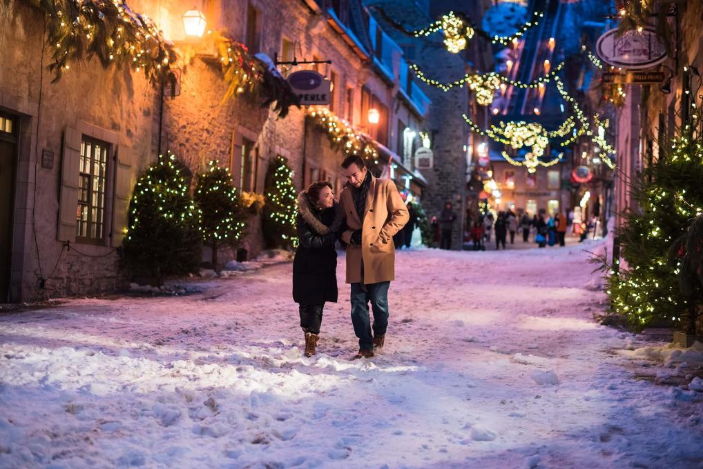 Couple marchant dans la rue Sous-le-Fort enneigée dans le quartier Petit-Champlain, avec les décorations illuminées de Noël. 