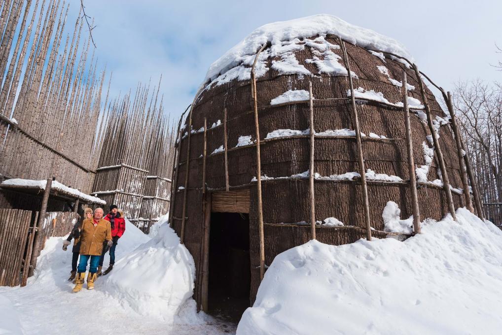 A couple walks outside the snowy longhouse with a guide, in Wendake near Québec City.