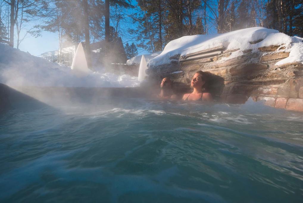 A couple relax in an outdoor spa in winter.