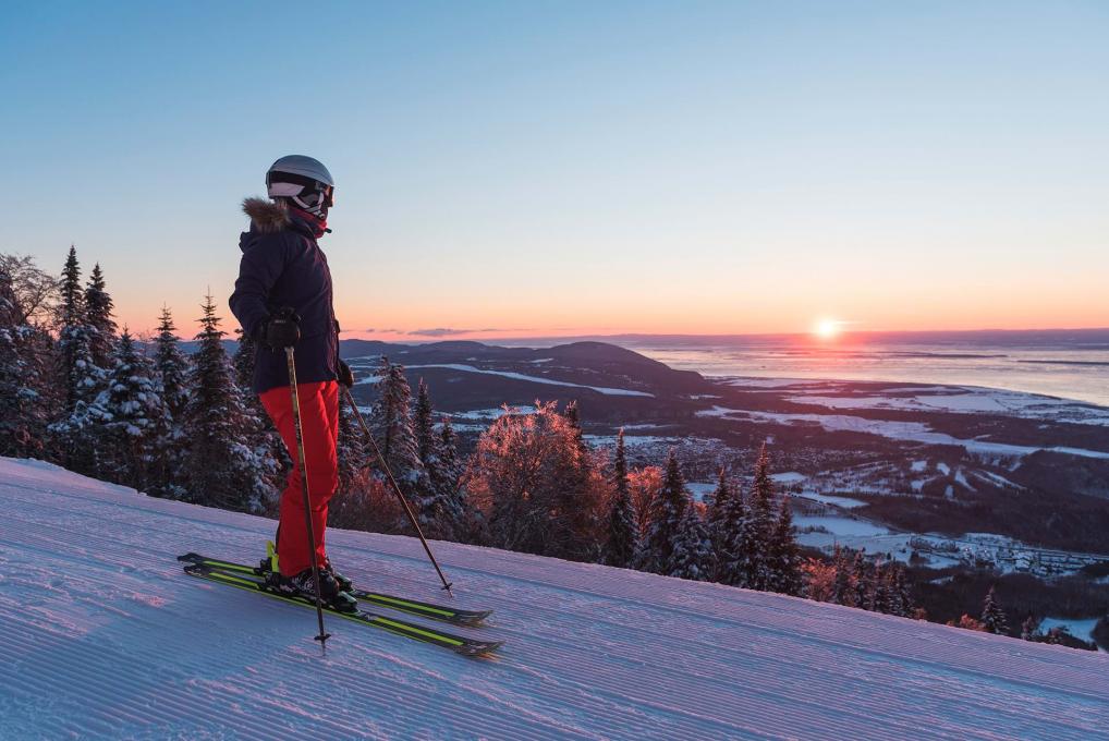 Une skieuse observe le coucher du soleil au sommet d'une montagne à la station de ski alpin du Mont-Sainte-Anne. 