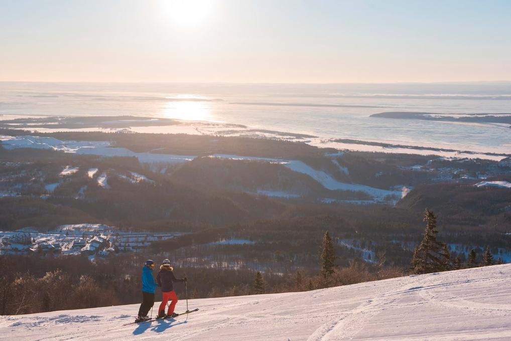 Deux skieurs observent le fleuve Saint-Laurent au somment d'une montagne de ski au Mont-Sainte-Anne. 