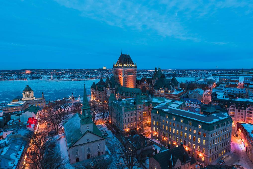 Vue aérienne du Vieux-Québec illuminé en début de soirée, avec le Château Frontenac, le fleuve et l'église Holy Trinity, en hiver.