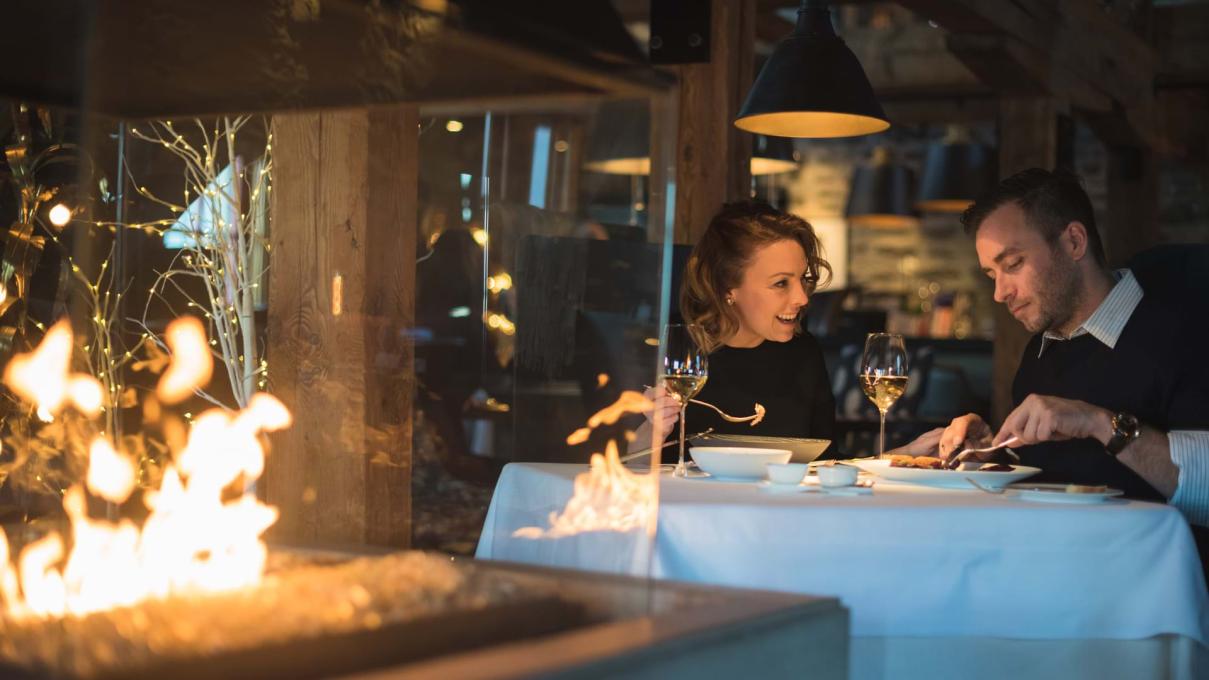 A couple enjoy a gourmet meal at Chez Muffy restaurant, in front of a fireplace.