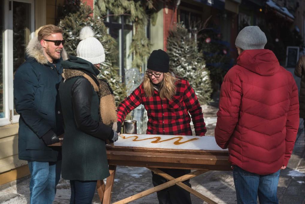 Trois passants s'arrêtent dans le quartier Petit-Champlain pour déguster de la tire sur neige dans une petite cabane à sucre.