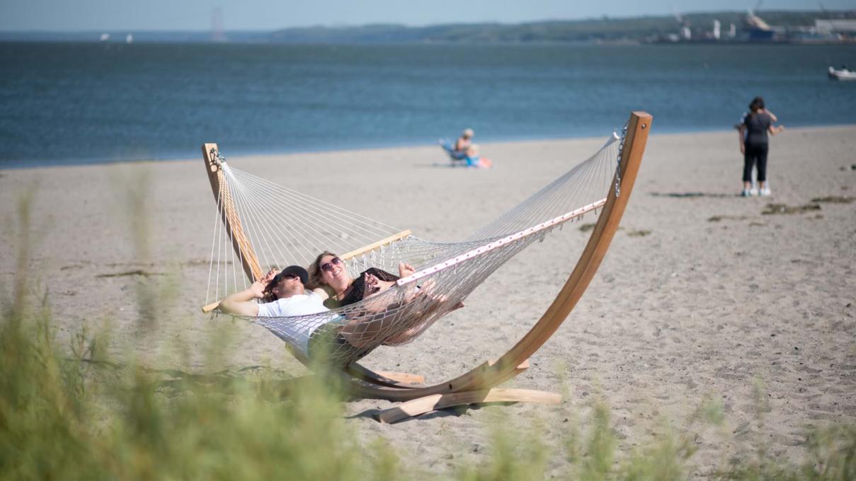A couple relaxes under the sun, in a hammock, on the beach at Baie de Beauport.