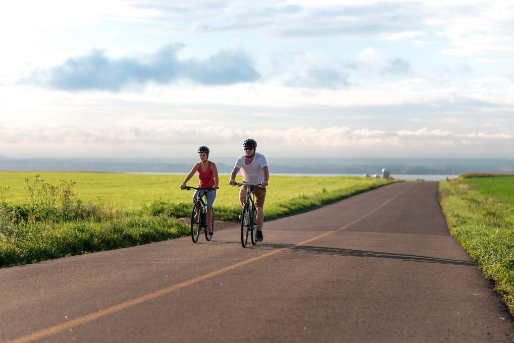 A couple rides a bicycle on a deserted road that runs alongside fields on Ile d'Orleans.