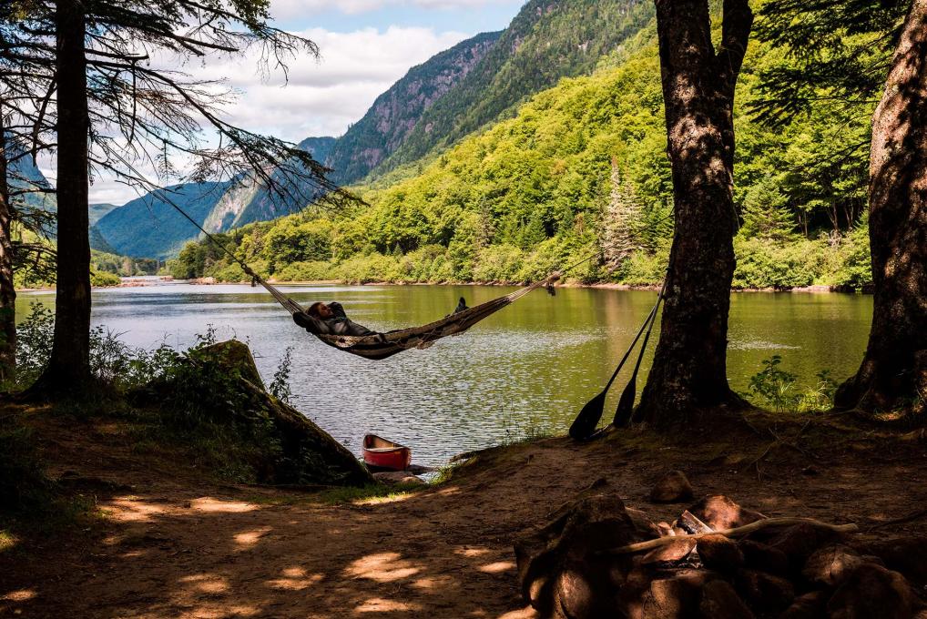 A man takes a nap in a hammock hanging from the trees on the riverside in Jacques-Cartier National Park.