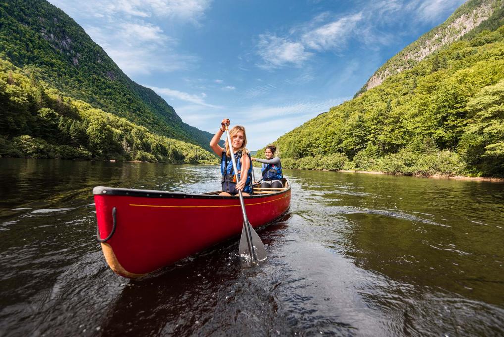 Two young women canoe in the river at the bottom of the valley, in Jacques-Cartier National Park.