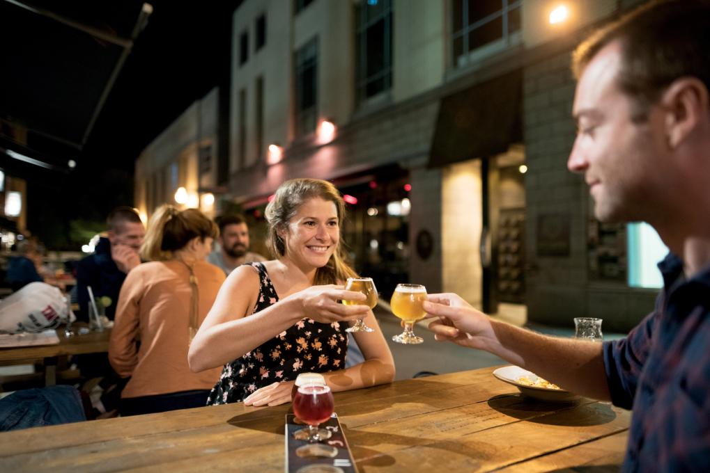 Un couple déguste des bières de microbrasserie sur une terrasse, en soirée.