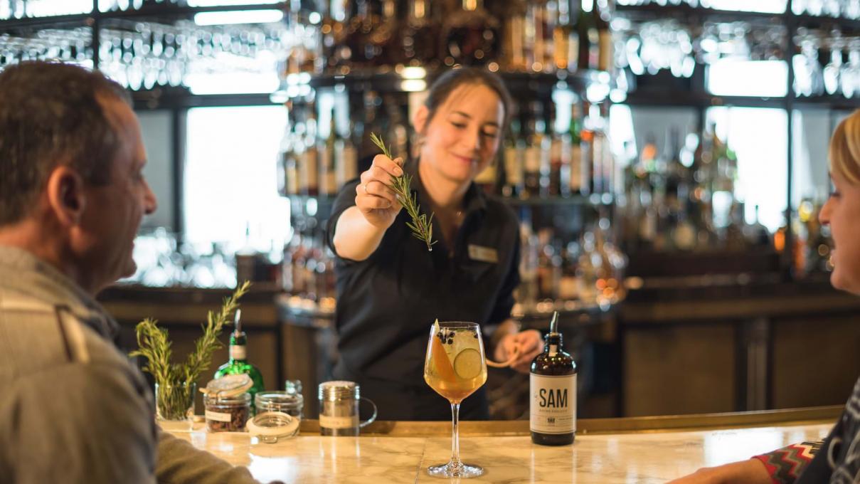 Une barmaid sert de l'alcool à un couple assis au au bar du restaurant Le Sam, de l'hôtel Fairmont Le Château Frontenac. 