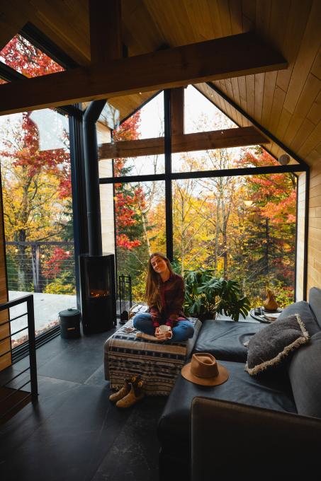 Femme dans un chalet tout fenestré sur l'automne