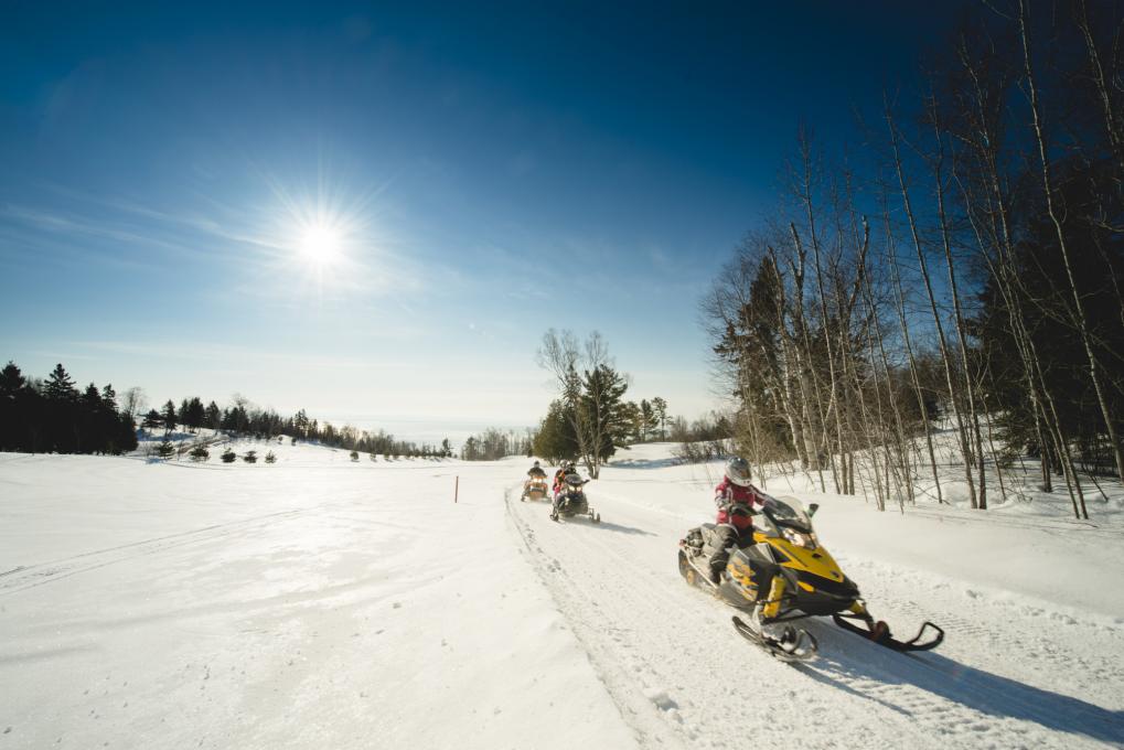 Snowmobilers riding across a snowy field in Charlevoix