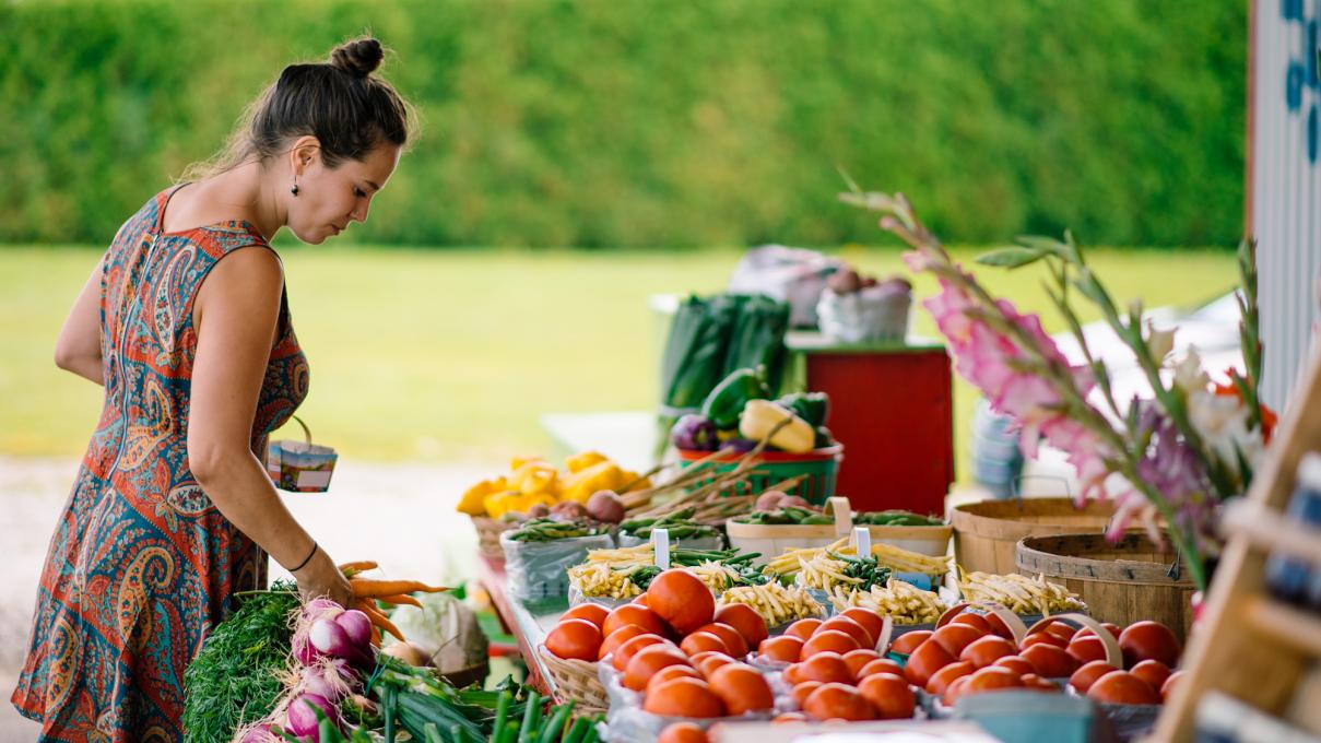 Un femme achète des fruits et des légumes frais dans un kiosque extérieur.
