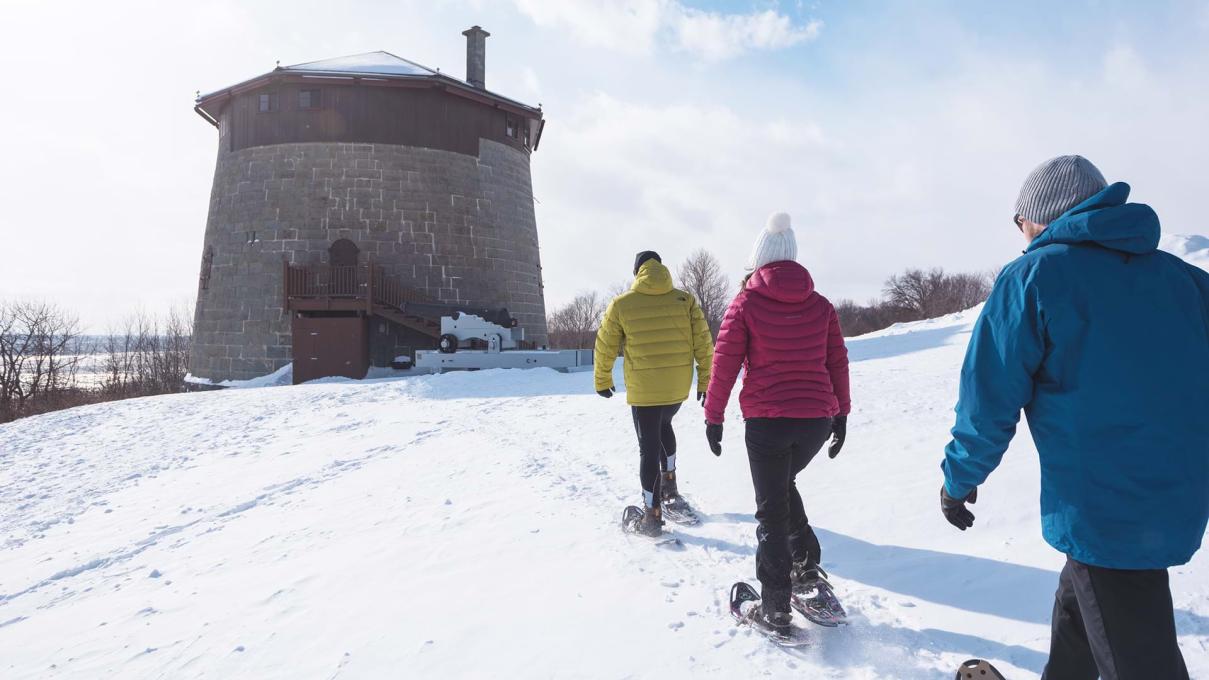 Three snowshoe hikers on the Plains of Abraham are heading towards Martello Tower no.1.