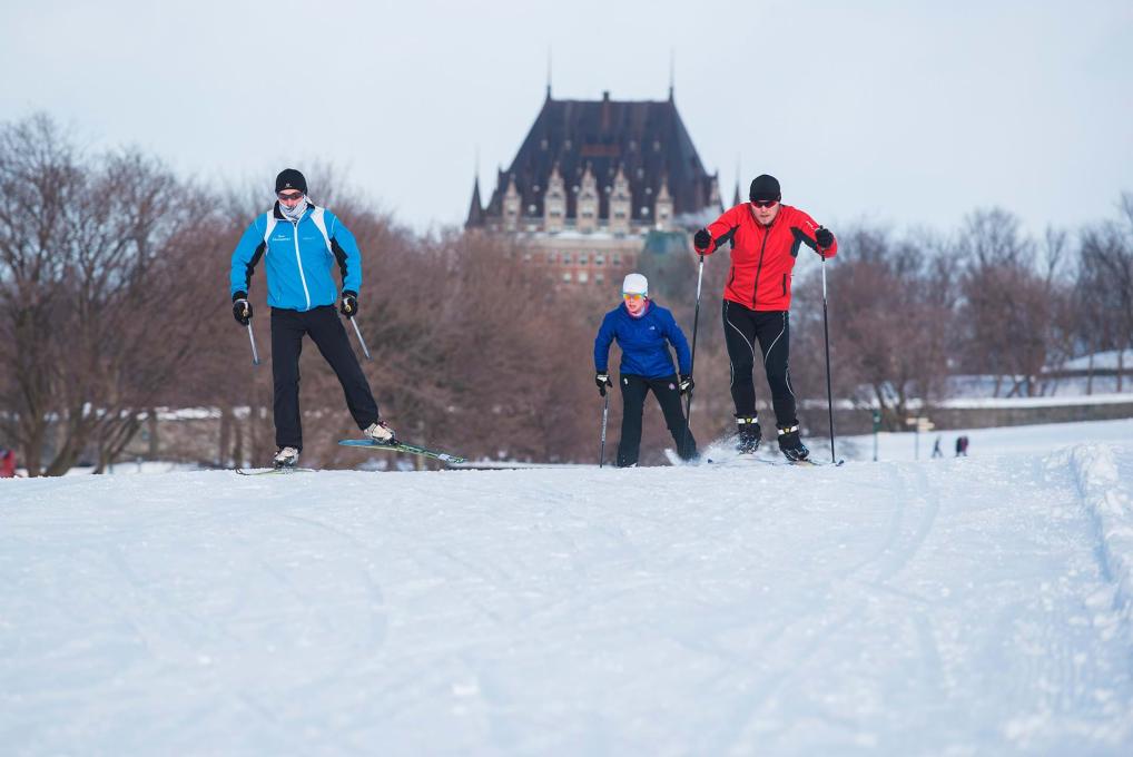 Trois skieurs pratiquent le ski de fond sur les plaines d'Abraham avec le Château Frontenac en arrière-plan.