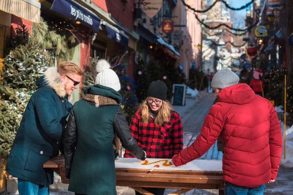 Three passers-by stop to taste maple taffy in the Petit-Champlain district.
