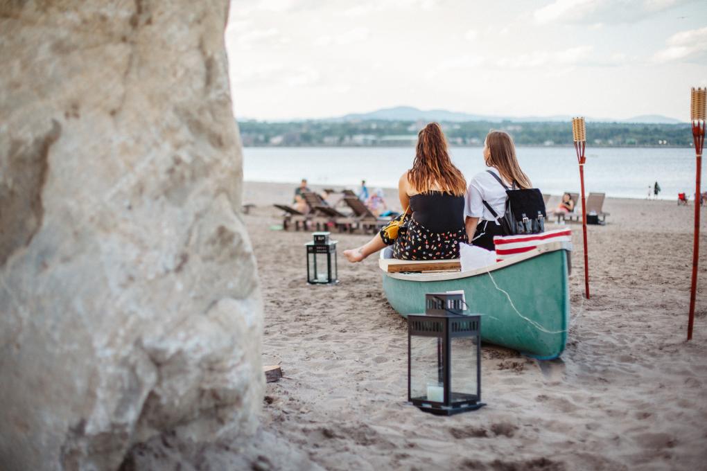 Two girls relax near a canoe on the beach at Baie de Beauport.