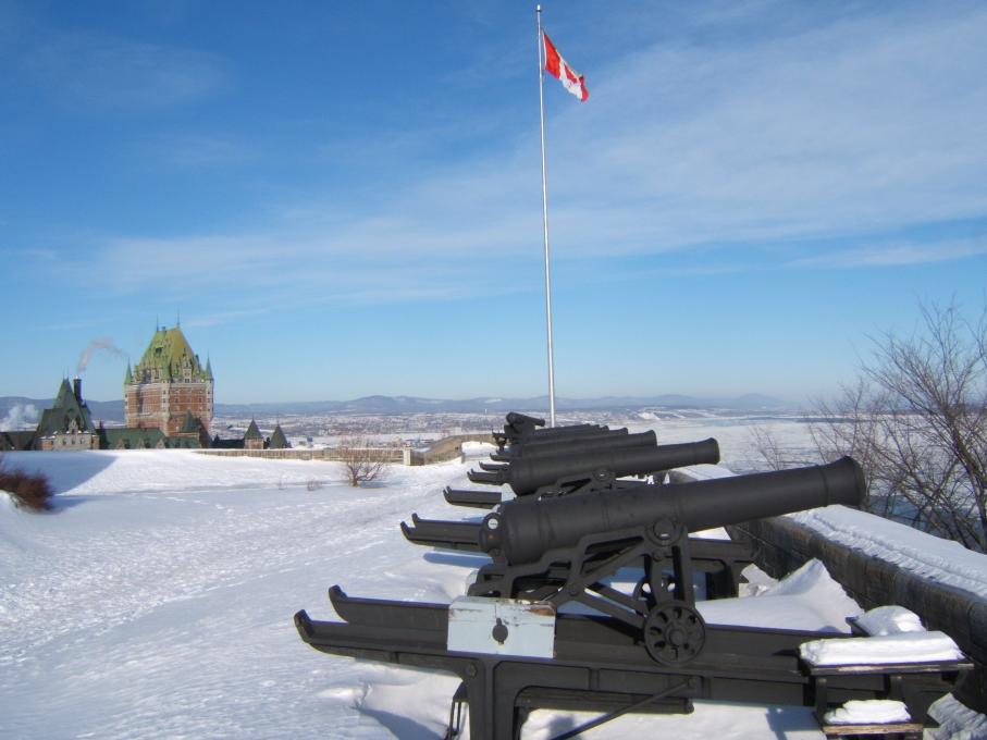 Several cannons in winter, in the snowy exterior courtyard of La Citadelle de Québec, with a view of the Château Frontenac.