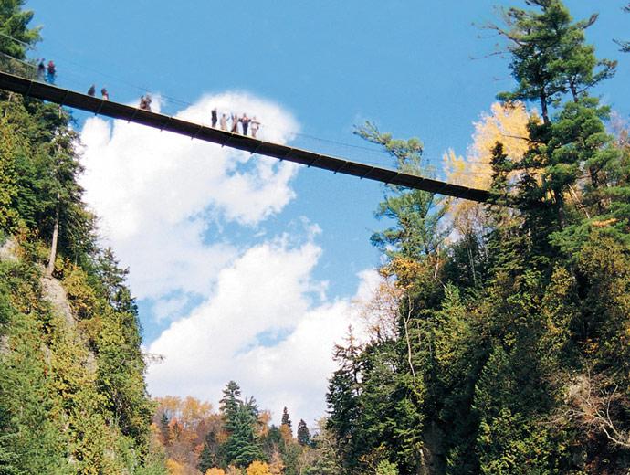 Des personnes traversent le pont suspendu au Canyon Sainte-Anne, en automne.
