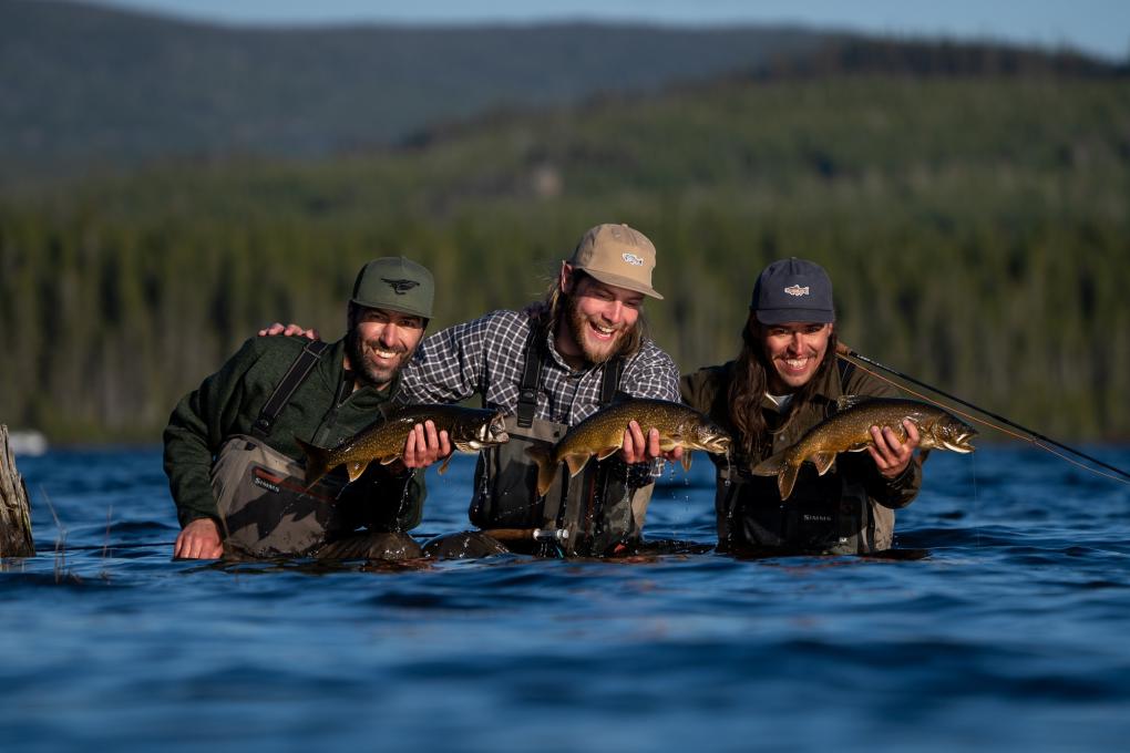 À la pêche dans la Réserve faunique des Laurentides, trois amis montrent fièrement leurs prises, au milieu d'un cours d'eau, par une belle journée ensoleillée d'été.