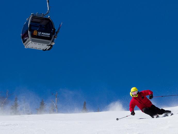 A skier descends an alpine ski slope under a cable car in the Massif de Charlevoix.