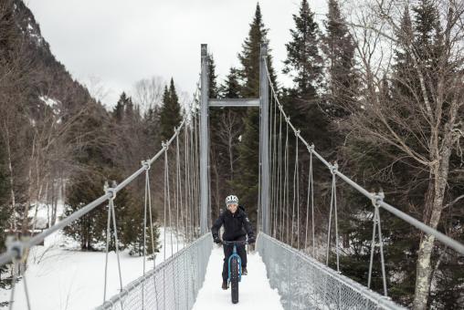 Un cycliste fait une randonnée en fatbike et traverse une passerelle enneigée dans la Vallée Bras-du-Nord.