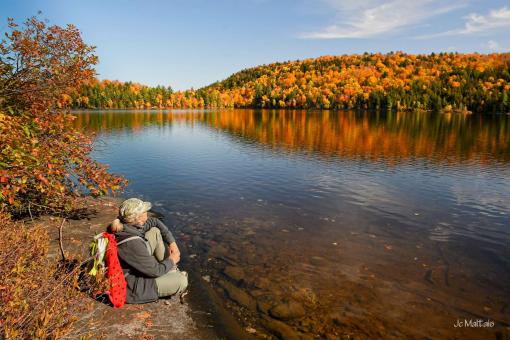 A person hiking contemplates Lake Carillon and the autumn landscapes in the Parc naturel régional de Portneuf.