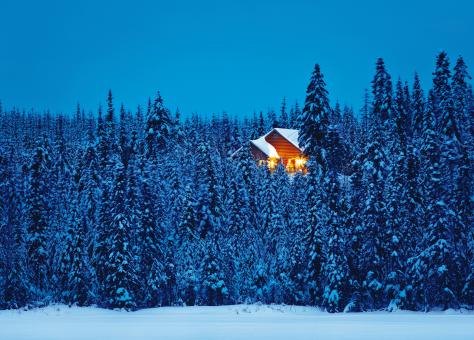 Exterior view of an illuminated chalet in the heart of a snowy forest, in the Réserve faunique des Laurentides, in winter.