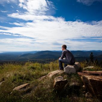 Un homme est assis et observe le panorama dans le sentier La Crête au Mont-Sainte-Anne.