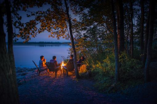Friends around a campfire, near a lake in the Réserve faunique des Laurentides, in the early evening, in summer.