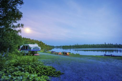 Couple relaxant autour du feu, sur leur emplacement de camping sur le bord d'un lac, dans la Réserve faunique des Laurentides, en été.