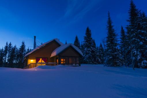 Exterior view of an illuminated chalet in the Réserve faunique des Laurentides, in winter.