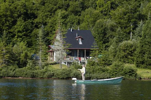A house by the water and a fisherman in a rowboat in the Portneuf Wildlife Reserve.