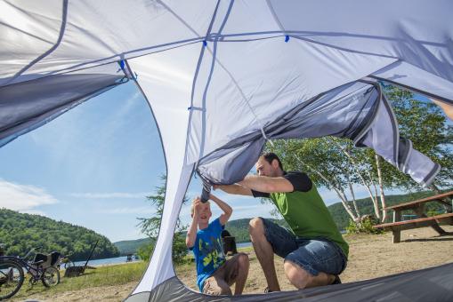 Un père et son enfant montent une tente sur un terrain de camping près d'un plan d'eau dans la Réserve faunique de Portneuf.