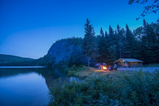 Des vacanciers autours d'un feu de camp en soirée, près d'un lac, dans la Réserve faunique de Portneuf.