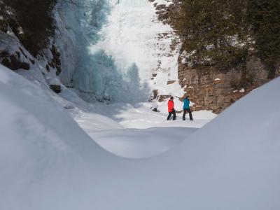 Two hikers walk in the snow at the foot of an icy waterfall, near Québec City.