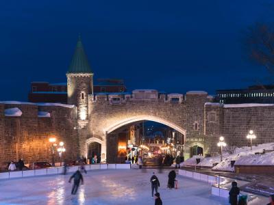 Porte Saint-Jean illuminated in the evening and skating at the Place D'Youville ice rink.