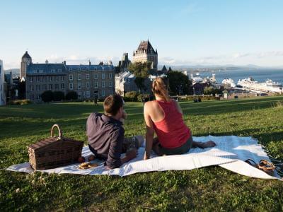 Couple picnicking near the Pierre-Dugua-De Mons terrace while admiring the Château Frontenac and the St. Lawrence River.
