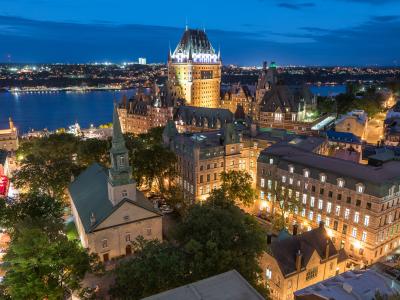 Aerial view of the illuminated Château Frontenac and the Holy Trinity Church in the early evening. 