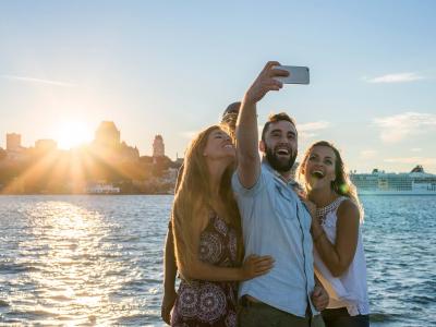 Groupe d'amis se prenant en photo au coucher du soleil, près du fleuve à Lévis avec un panorama du Vieux-Québec à l'arrière. 