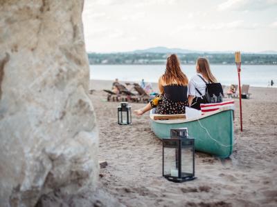 Two girls relax near a canoe on the beach at Baie de Beauport.