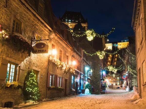 Rue Sous-le-Fort enneigée dans le quartier Petit-Champlain, avec les décorations illuminées de Noël. 