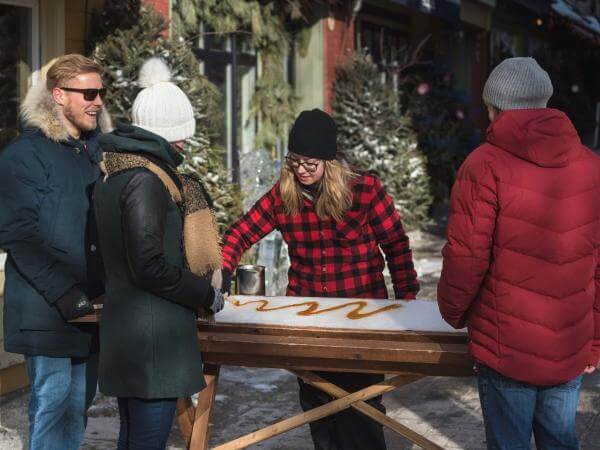 Three people stop in the Petit-Champlain district to taste taffy on snow in a small sugar shack.