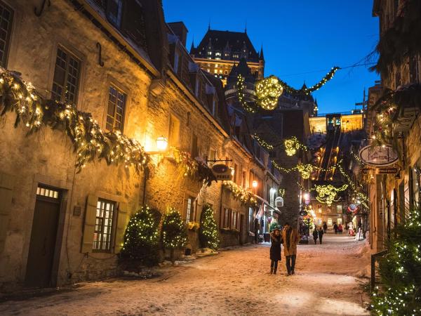 Un couple amoureux marche en soirée dans la rue du Petit-Champlain illuminée pour Noël et le temps des fêtes. 